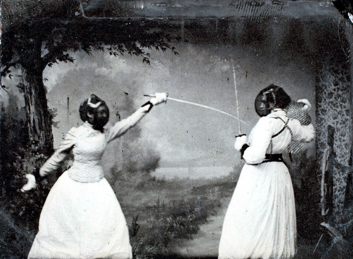 A black and white photo of two figuresin white dresses wearing fencing masks and using those fencing thingies to, uh, fence.
