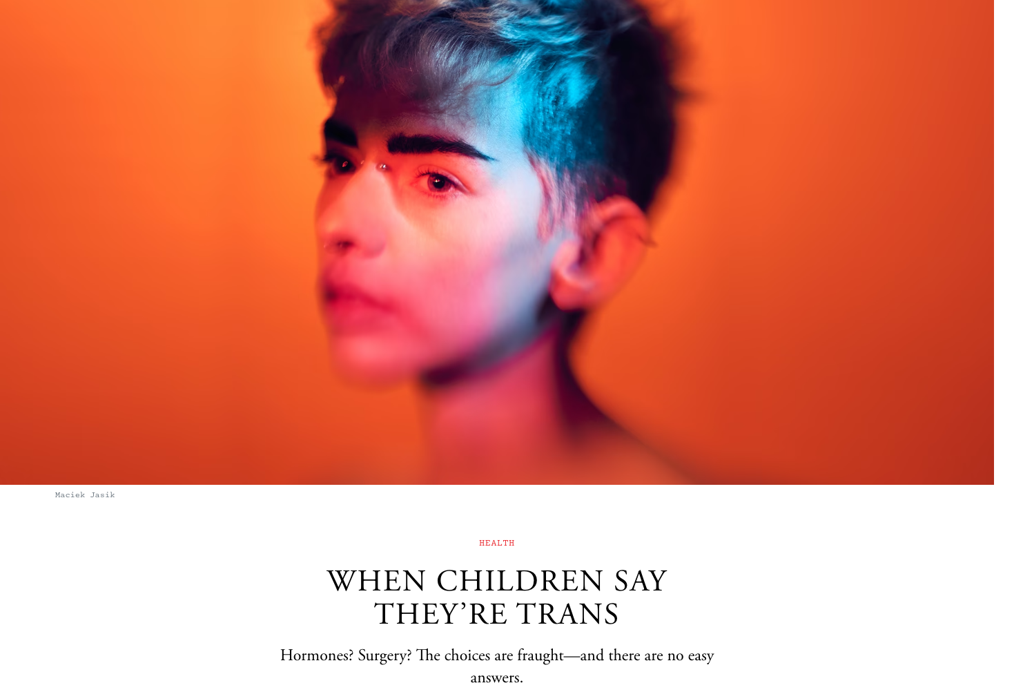 A non-binary youth in red and blue light looks off camera with a pensive look.
